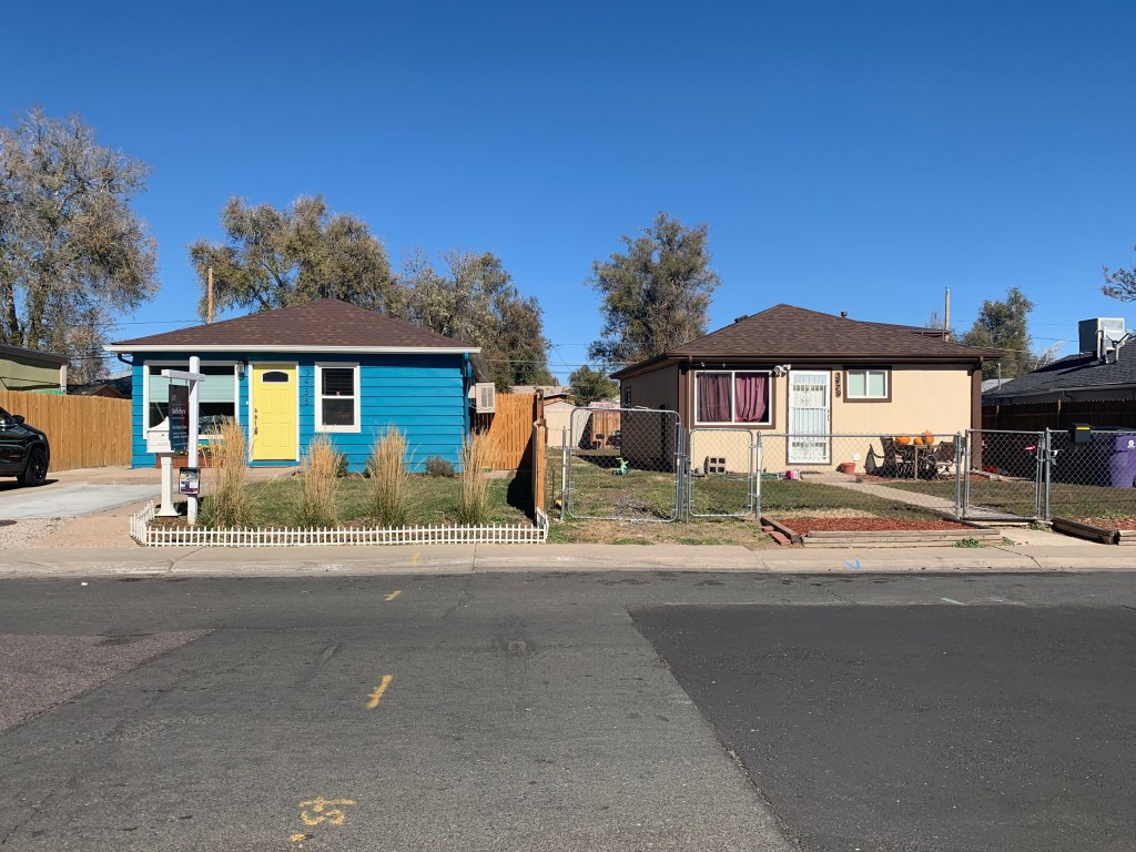 Two small one-story homes are pictured from the street, one painted bright blue with a yellow door, new landscaping, and a for sale sign; the other has shades drawn across the windows and a chain link fence.  